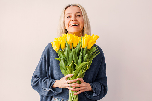Adult woman at home mother's day concept holding tulips bouquet smiling. Beautiful middle aged female celebrating birthday, smelling bouquet of flowers at home