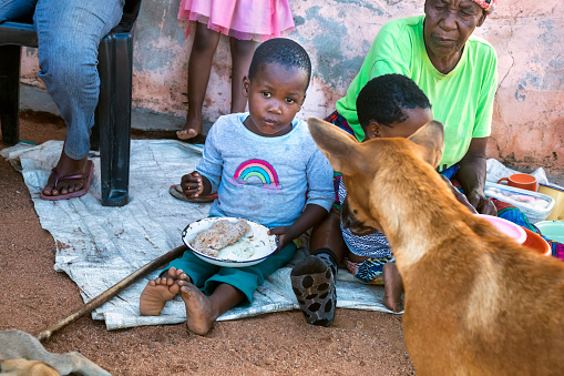 Small African child eating with hands from the plate on the ground