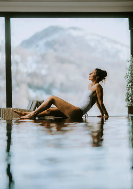 Young woman relaxing on the poolside of infinity swimming pool at winter time stock photo