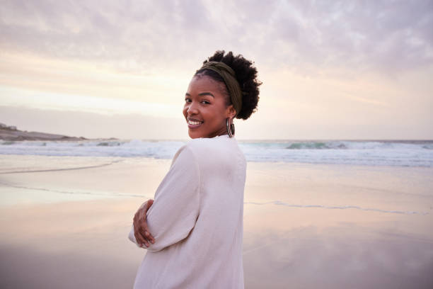istock Young woman smiling while watching sunset on a beach in summer 1392324337