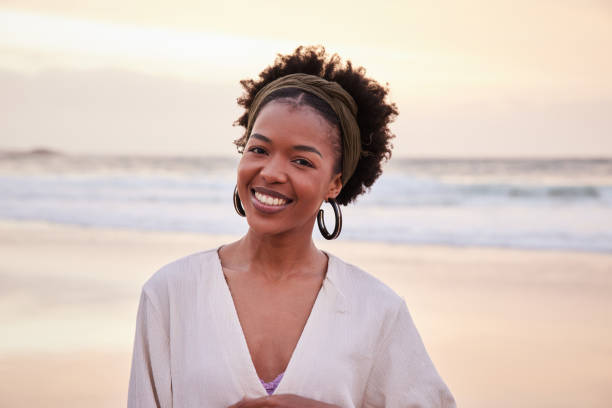 istock Young woman smiling while standing on a sandy beach at sunset 1392325068