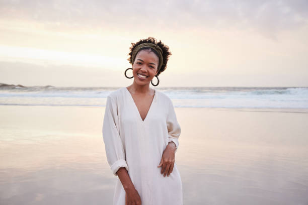 istock Smiling young woman standing on a sandy beach at sunset 1392325165