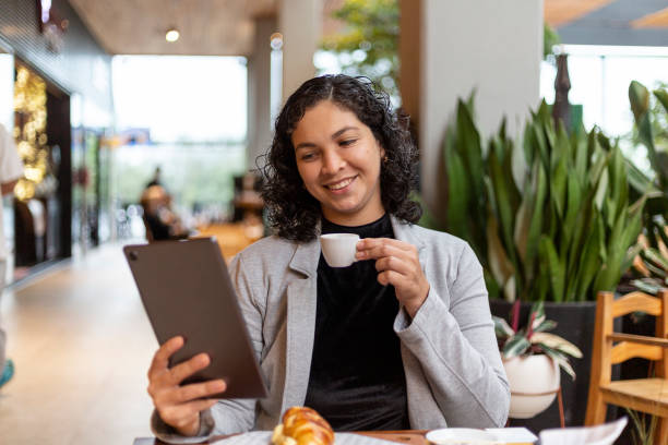 istock Curly haired latin woman in her 30s using tablet in a cafe and working 1392325177