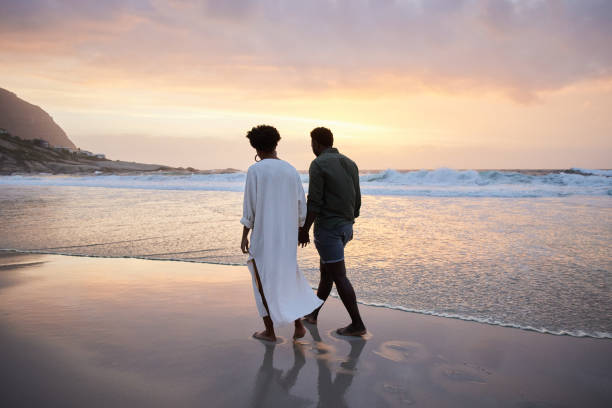 istock Young couple walking hand in hand on a sandy beach at dusk 1392325363