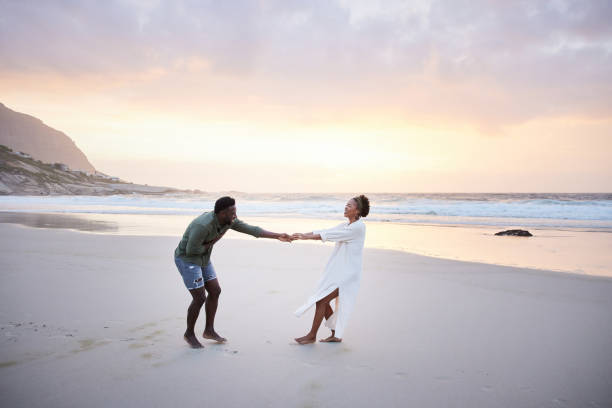 istock Laughing young woman pulling her husband along a beach at sunset 1392325402