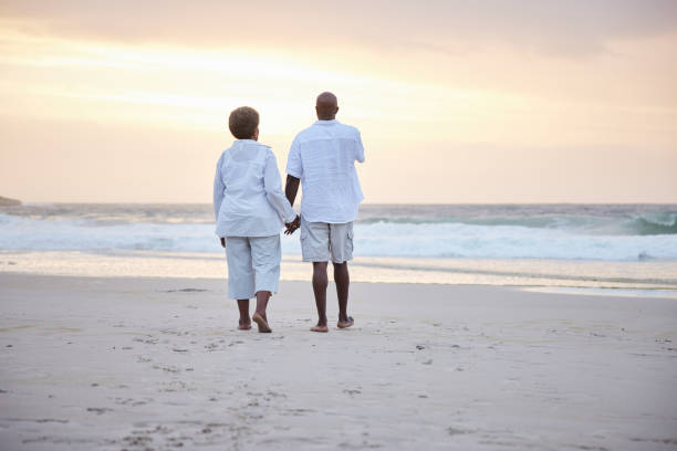 istock Senior couple walking hand in hand on a beach at sunset 1392325497