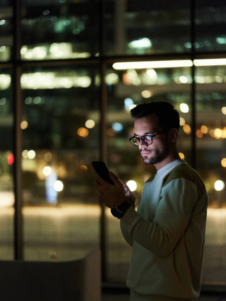 istock Young man text messaging on cell phone indoors at night. 1392325704
