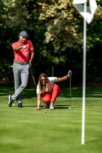 casal jogando golfe, jovem mulher lendo verde, preparando-se para colocar - golf course fotos - fotografias e filmes do acervo