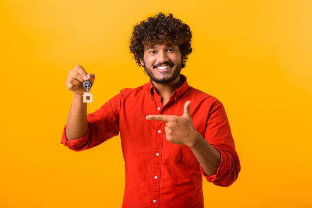 istock Smiling middle eastern man holding keys from new property and pointing with finger on it. Happy buyer of own estate 1392326406