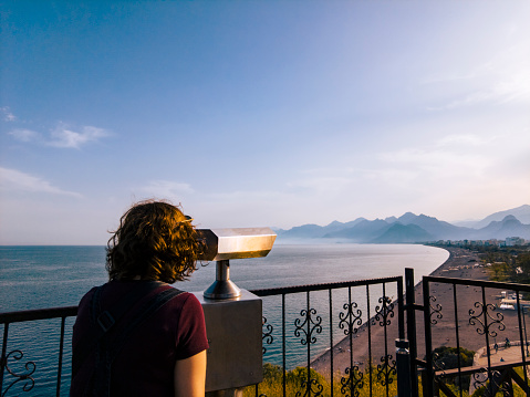 Tourist watching distant mountain and sea view through city binoculars