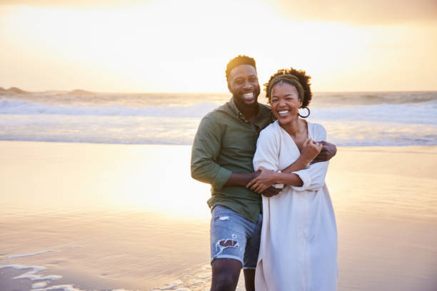 istock Laughing young couple standing on the beach at sunset 1392326615