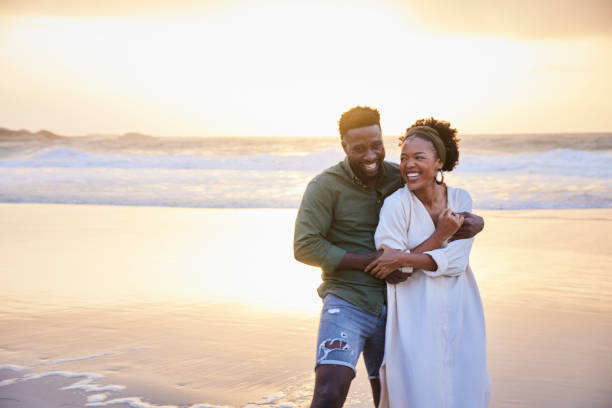 istock Laughing young couple standing on the beach at sunset 1392326646