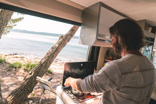 istock Man cooking in a camper-van, ocean view 1392326684