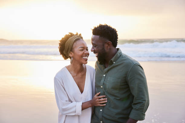 istock Laughing young couple standing on a sandy beach at sunset 1392326888