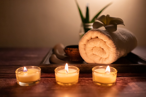 Close up wooden Gun Sha, rolled towel, stone, flower and candle on the tray over wooden background. Facial spa set, wellness well-being lifestyle concept.
