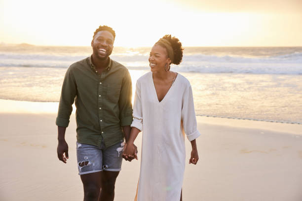 istock Young couple laughing while walking hand in hand on a beach at sunset 1392328364