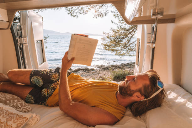 istock Man lying at the back of a van reading a book 1392328390