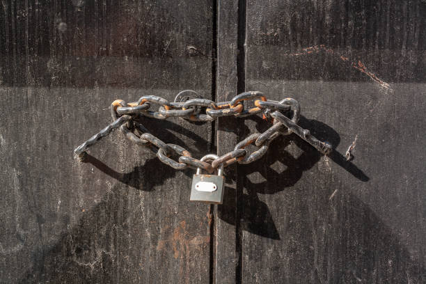 istock Thick chain with closed lock is threaded through the iron handles on iron door. Black dirty door. Horizontal photo. 1392329435