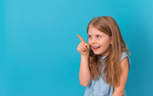 istock Little smiling girl pointing on copy-space on blue background. 1392331220