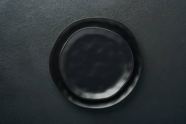 istock Ceramic empty black plate on old black ceramic cement concrete table background. Cooking stone backdrop. Top view with copy space. Flat lay 1392335119