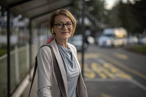 Woman waiting for a bus Portrait of a mature businesswoman standing at the bus stop outdoors in city. older woman purse stock pictures, royalty-free photos & images