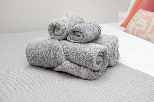 White towels stacked on a bed. The towels are all the same size and shape, and they are made of a soft, absorbent material. The towels are stacked neatly, with the edges aligned.
