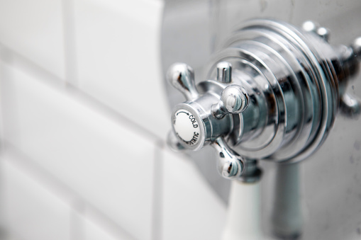 Extreme close-up of chrome hot and cold shower handle on a white tile wall