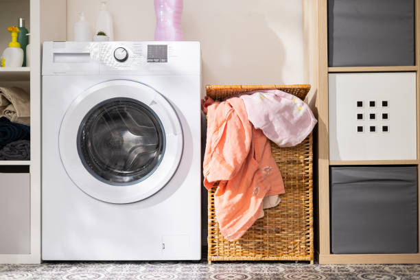 istock Washing machine in laundry room with wicker basket for dirty clothes packed full 1392335560
