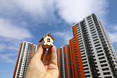 Wooden house model in male hand on background of new buildings and blue sky