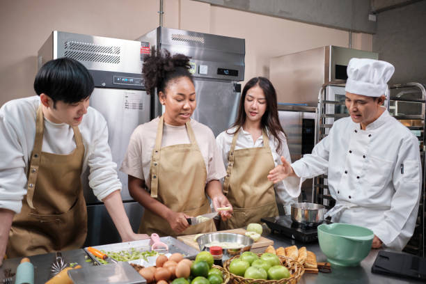 Senior chef teaches young cooking students to peel fruits in culinary courses. stock photo