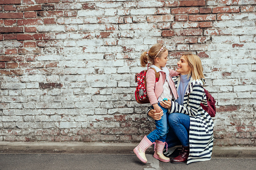 Adorable little girl with schoolbag and her mother in a warm embrace out in the city