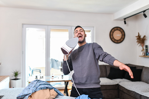 Happy Male Singing With Clothing Iron While Finishing Home Chores