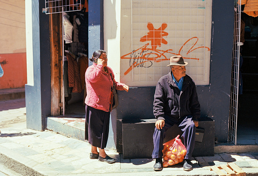 San Cristobal de las Casas, Mexico, February 11, 2022: Man in hat sitting near the entrance to the shop and woman talking on the phone near him