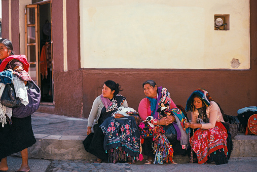 San Cristobal de las Casas, Mexico - February 11, 2022: Three women in Mayan clothes  sitting on the bench and selling traditional Mexican souvenirs