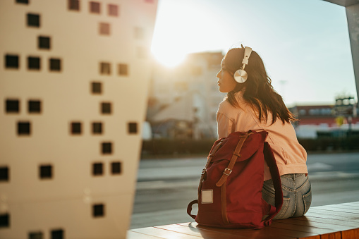 Asian woman listening to music while sitting and waiting for a bus