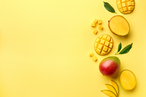 Fresh whole half and sliced mango fruit on yellow background, top view, flat lay, copy space for text