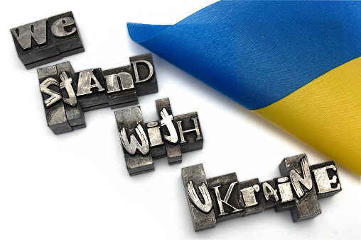 Close-up of a Ukrainian flag next to metal lead printing stamps letters representing we stand with ukraine on white background as a concept for solidarity and help during the war between Russia and Ukraine