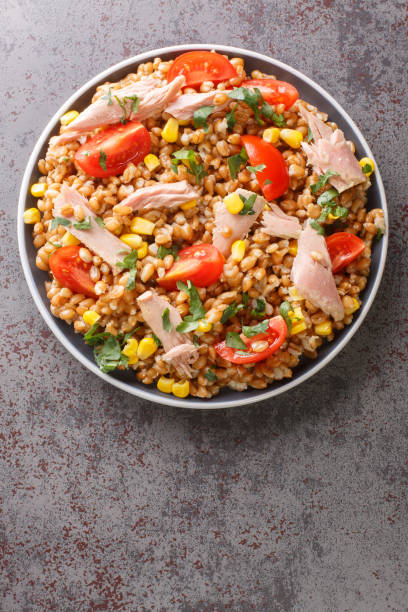 istock Boiled spelled with tuna, corn, tomatoes and herbs close-up in a plate. vertical top view 1392352154