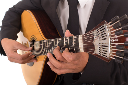 Close up shot of a man with his fingers on the frets of a portuguese guitar playing