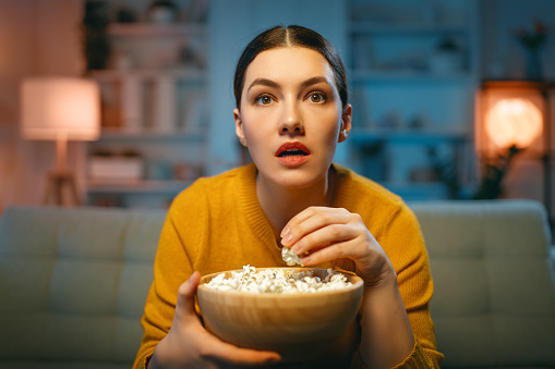 Young woman watching  TV, movies with popcorn. Girl spending time at home.