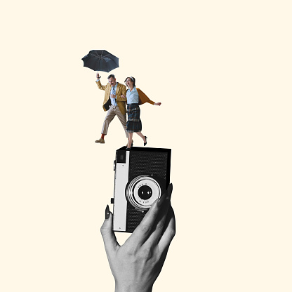 Contemporary art collage. Young loving couple with umbrella running on retro camera device isolated over light yellow background. Taking photos. Romantic date. Concept of vintage style, love, fashion