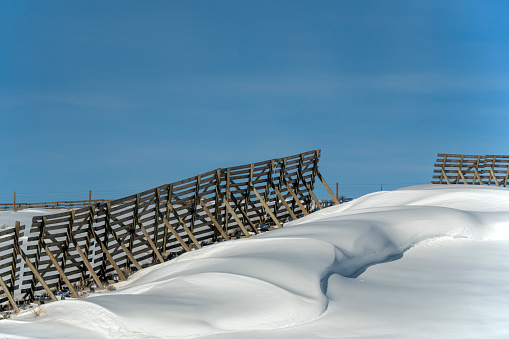 Wooden snow fence with snowdrift on downwind side. This fence is used to keep snow off of a road. Wyoming, USA.