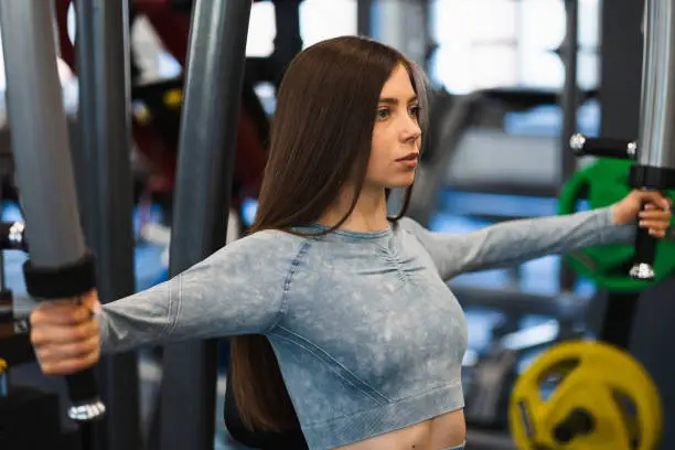 Close-up of a fit girl who exercises on a butterfly machine