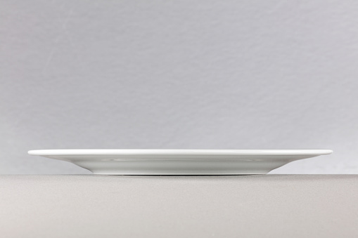 A side view of a white dinner plate on neutral background