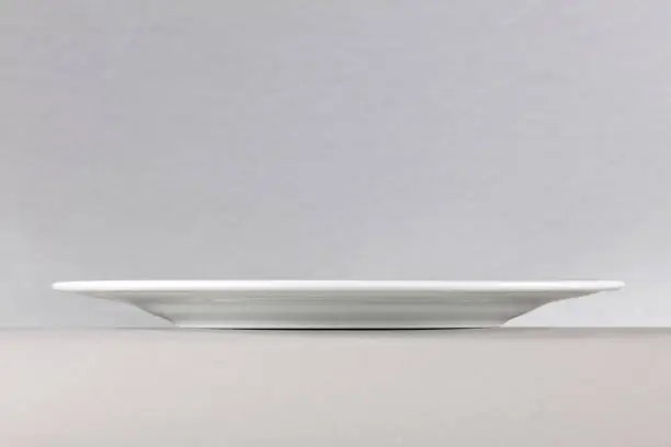 A side view of a white dinner plate on neutral background