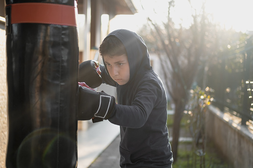 Handsome teenage boy doing fight workout punching heavy bag looking cool.