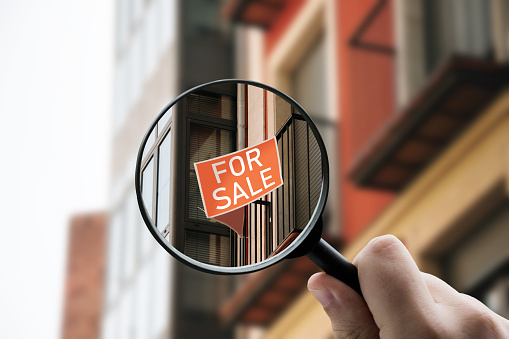 Magnifying glass focusing a 'For Sale' sign on an apartment building window