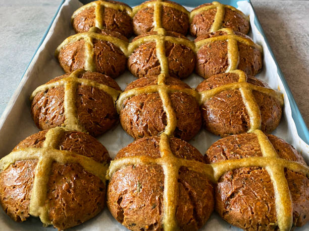 Stock photo showing an elevated view of greaseproof paper lined baking oven tray containing freshly baked, homemade, savoury, cheese and pesto hot cross buns, home baking concept.
These rolls are traditionally spiced sweet buns sold over the Easter period, with the cross symbol on the glazed top being made from a flour and water paste, and symbolising Christianity. imagen de primer plano de bollos cruzados calientes recién horneados, caseros y salados en una bandeja de horno de horno antiadherente forrada de papel pergamino a prueba de grasa, panecillos de queso y pesto, concepto de horneado casero, enfoque en prime