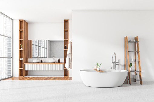 Light bathroom interior with tub on white concrete floor, sink with mirror and shelf with accessories. Panoramic window on city view. 3D rendering
