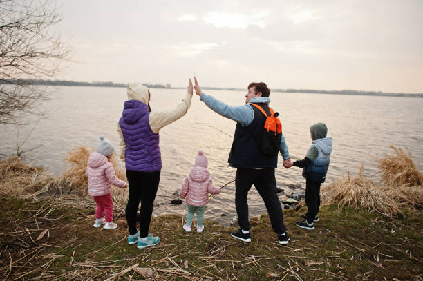Back of family with three kids on the shore of the lake. Husband gives his wife high five. Back of family with three kids on the shore of the lake. Husband gives his wife high five. big family sunset stock pictures, royalty-free photos & images